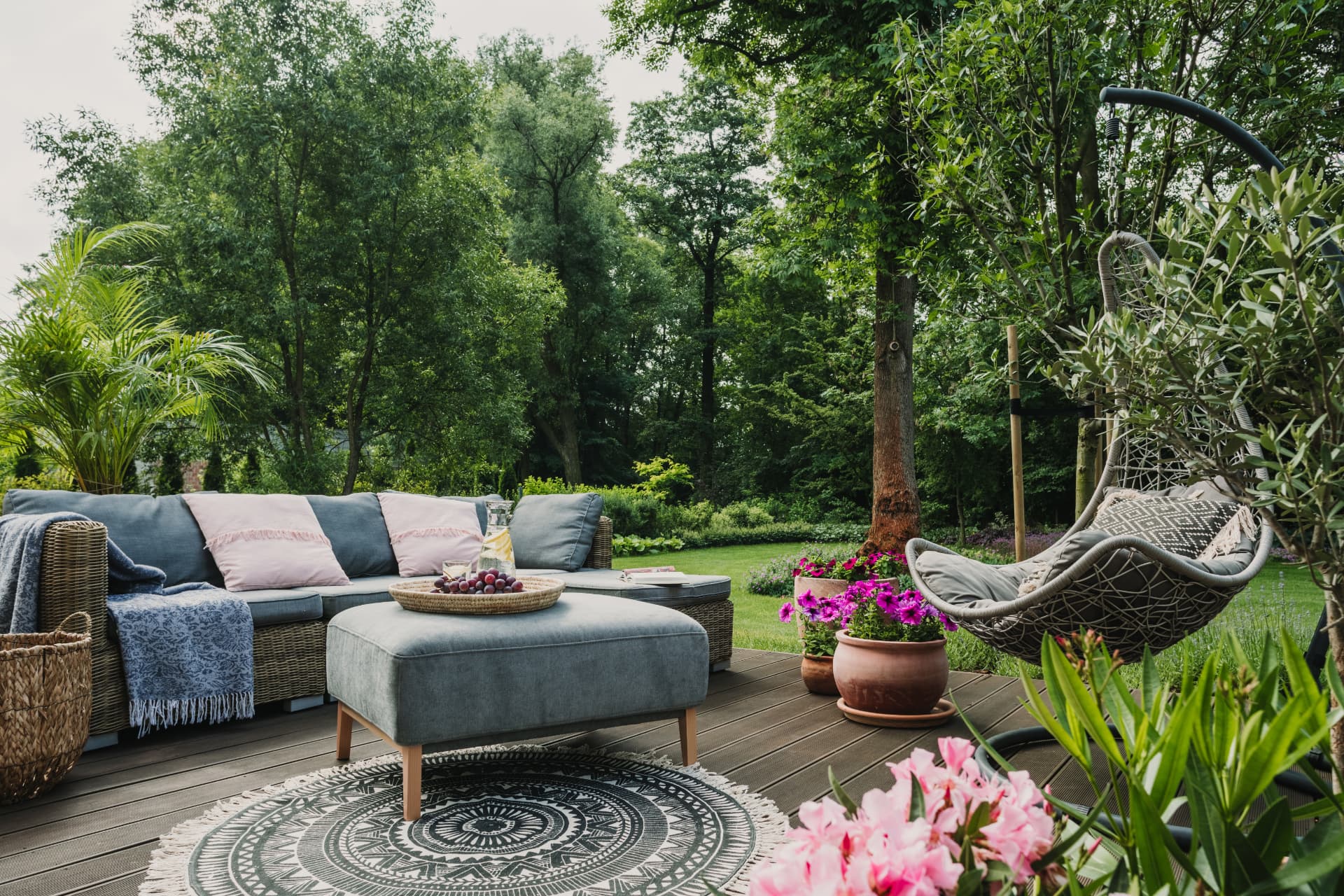 A timber deck with cushioned outdoor sofa, hanging chair and potted flowers beside a lawn